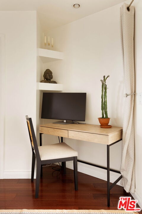 Home office nook with a light wood desk, black-framed chair, and potted cactus.