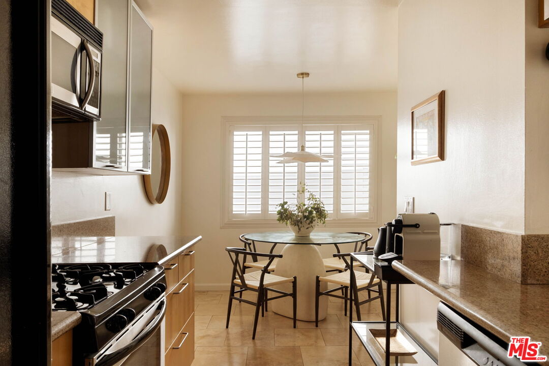 Kitchen and dining area with stainless steel appliances, a round table, and plantation shutters.