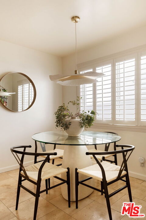 Dining area with a round glass table, woven chairs, and white plantation shutters.