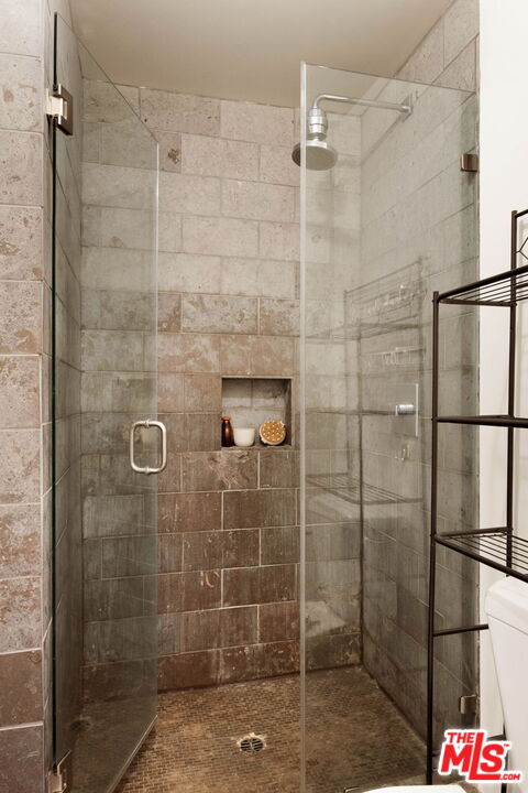 Walk-in shower with glass doors, stone tile, a built-in niche, and a rainfall showerhead.