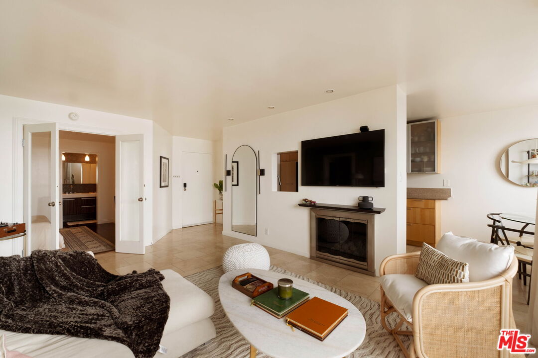 Furnished living room with a TV above the fireplace and an open kitchen behind it.