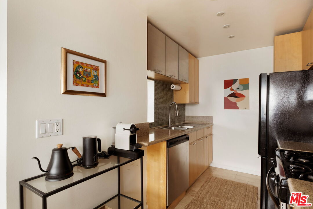 Galley kitchen with light wood cabinets, stone counters, double sink, and a coffee station.