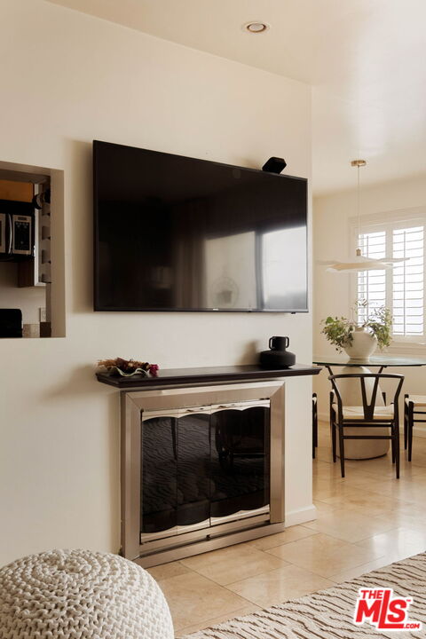 Living room with a television above the fireplace and a dining area by shuttered windows.