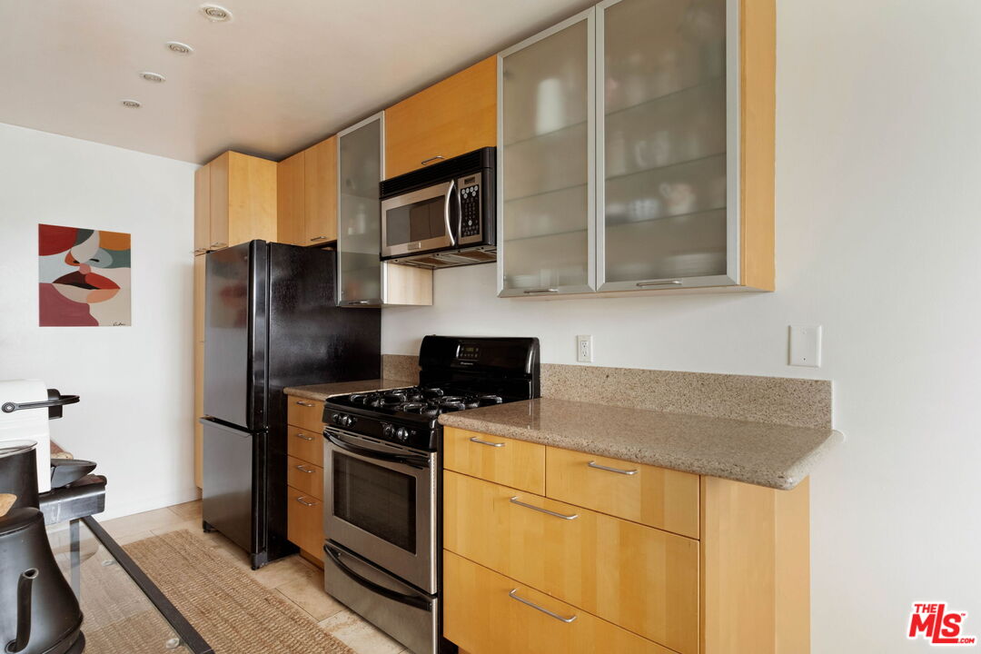 Condo kitchen with light wood cabinets, granite counters, and a black refrigerator beside a stainless steel range.