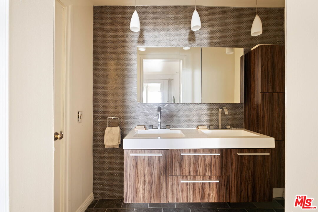 Bathroom with a double-sink wood-grain vanity, dark mosaic tile backsplash, and large mirror.