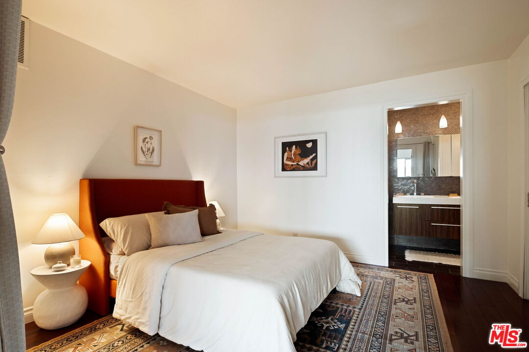 Furnished bedroom with a rust-colored headboard, patterned rugs, and an ensuite bathroom doorway.