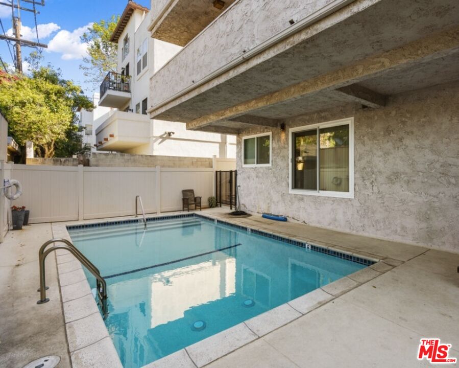 Courtyard swimming pool beside a residential building, enclosed by a white privacy fence.