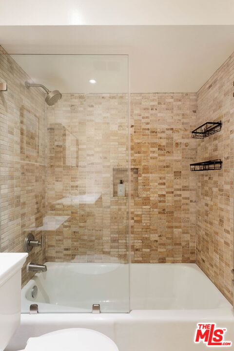 Bathroom with a tiled tub and shower, clear glass screen, chrome fixtures, and black wire shelves.