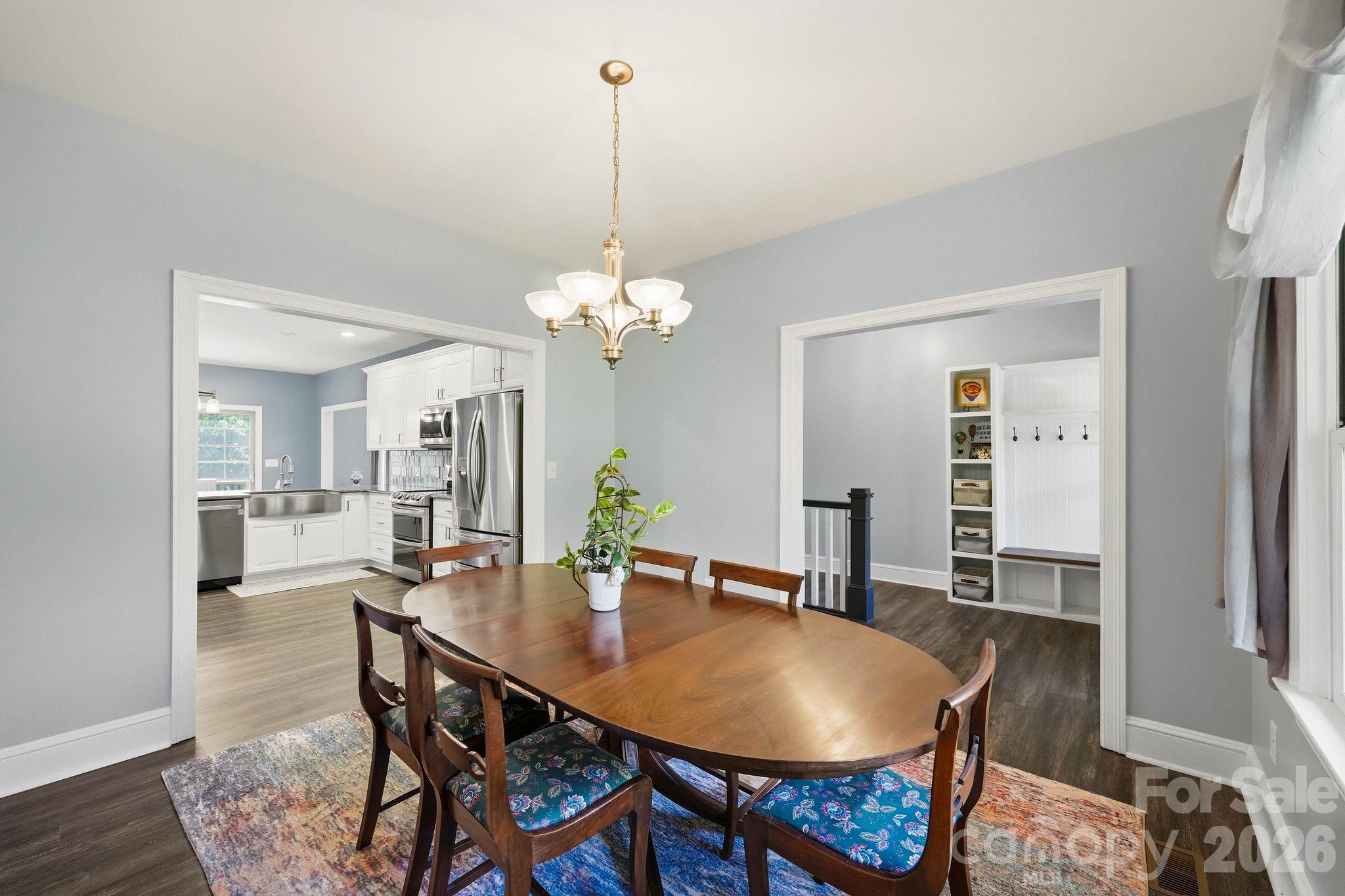 Dining room with an oval wood table and chandelier, opening to a white kitchen and built-in mudroom bench.