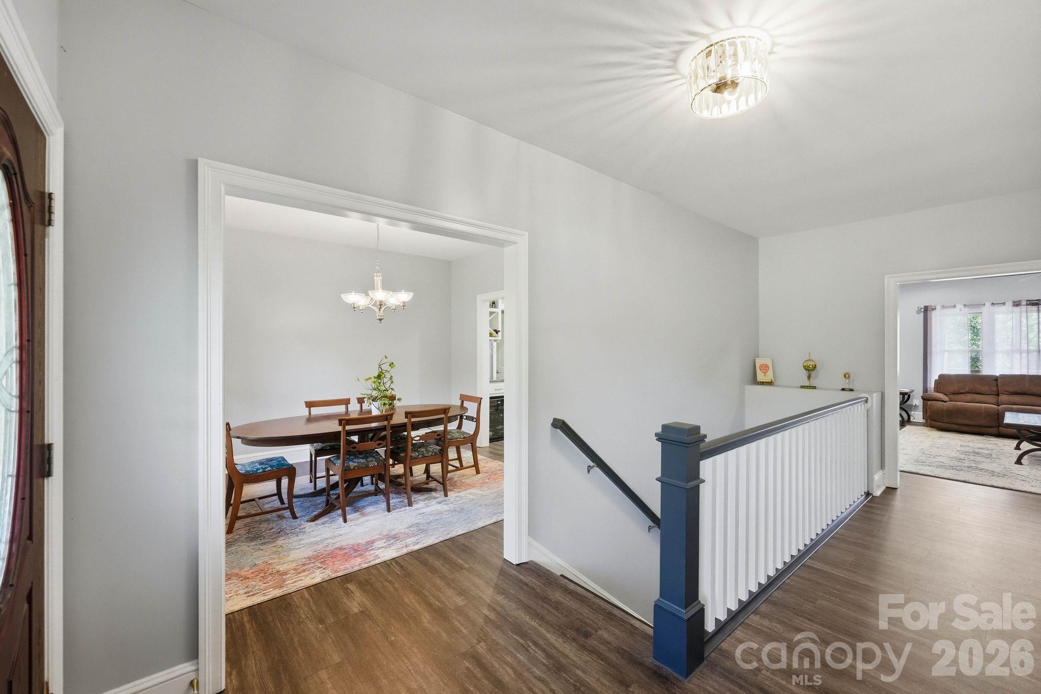 Upstairs landing with a navy-blue newel post, overlooking a furnished dining room and living room.