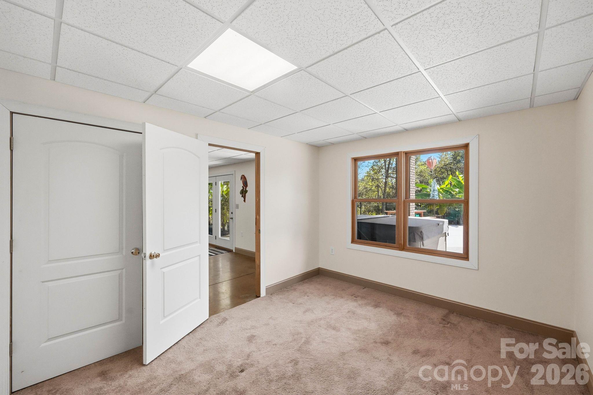 Empty carpeted room with an open door and a window overlooking a deck and hot tub.
