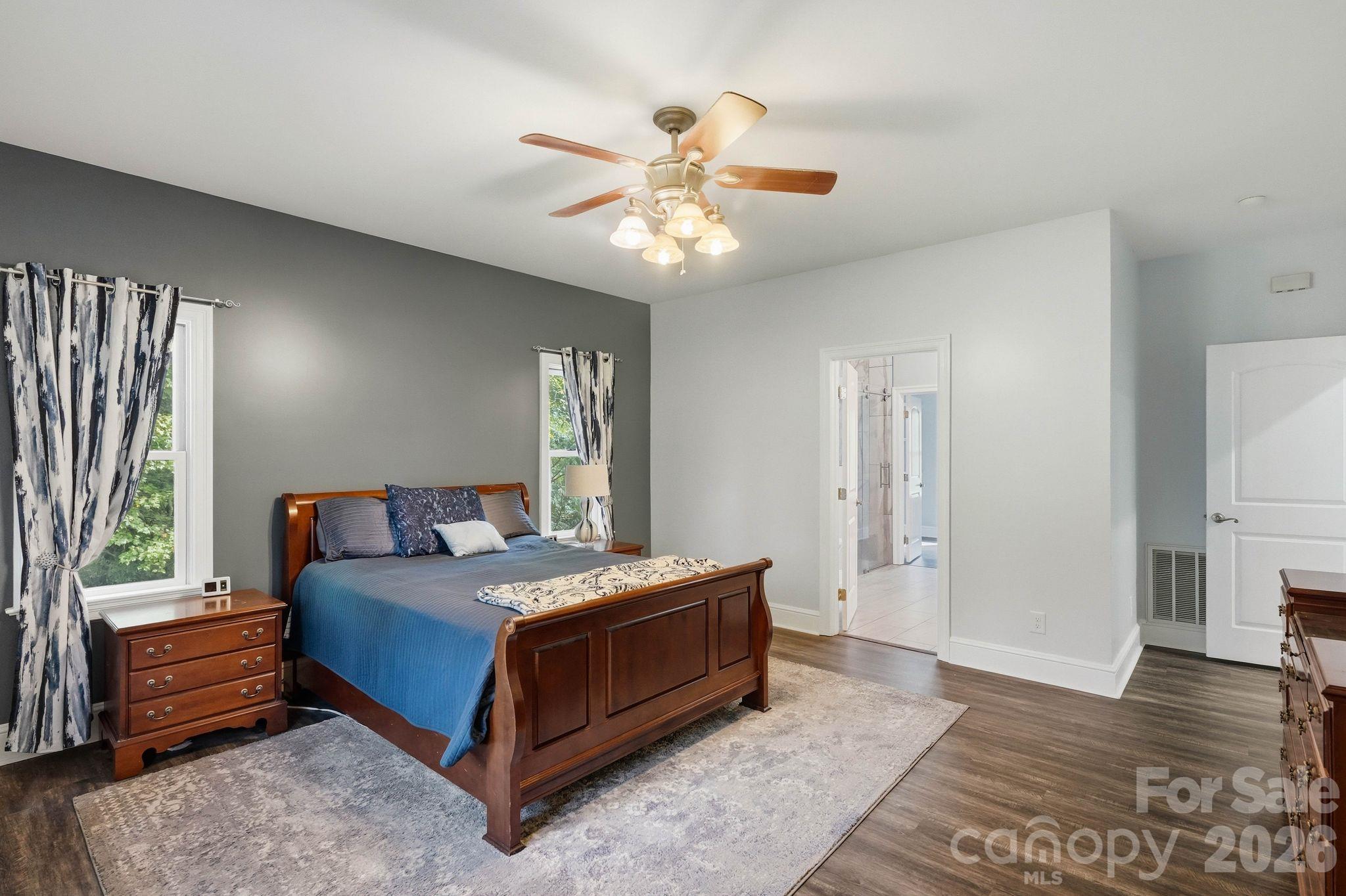 Bedroom with a dark wood bed, blue bedding, patterned curtains, and an open doorway to the bathroom.
