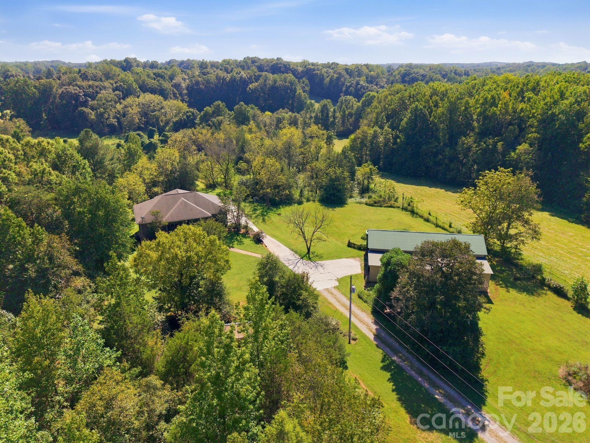 Aerial view of a house and outbuilding amid lawns and dense woodland.
