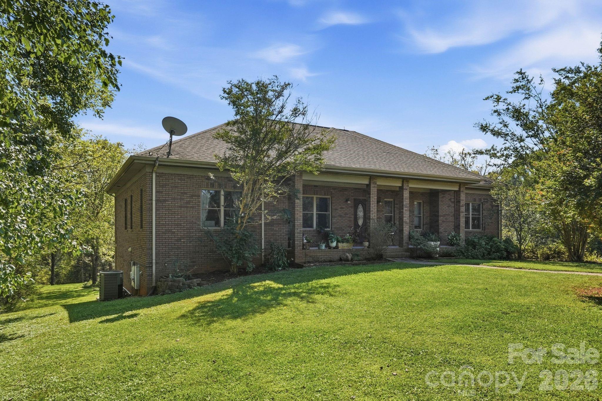 Brick house with a covered porch, surrounded by mature trees and a broad green lawn.