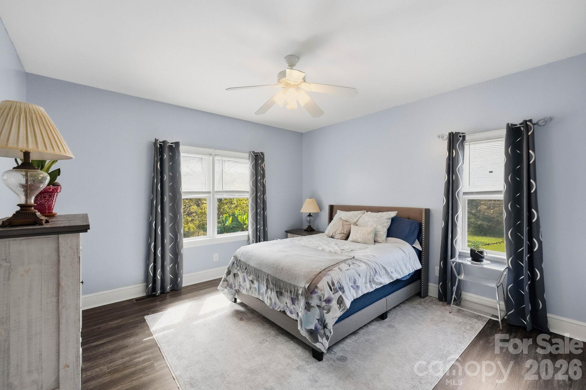 Furnished bedroom with a bed between two windows and a ceiling fan.