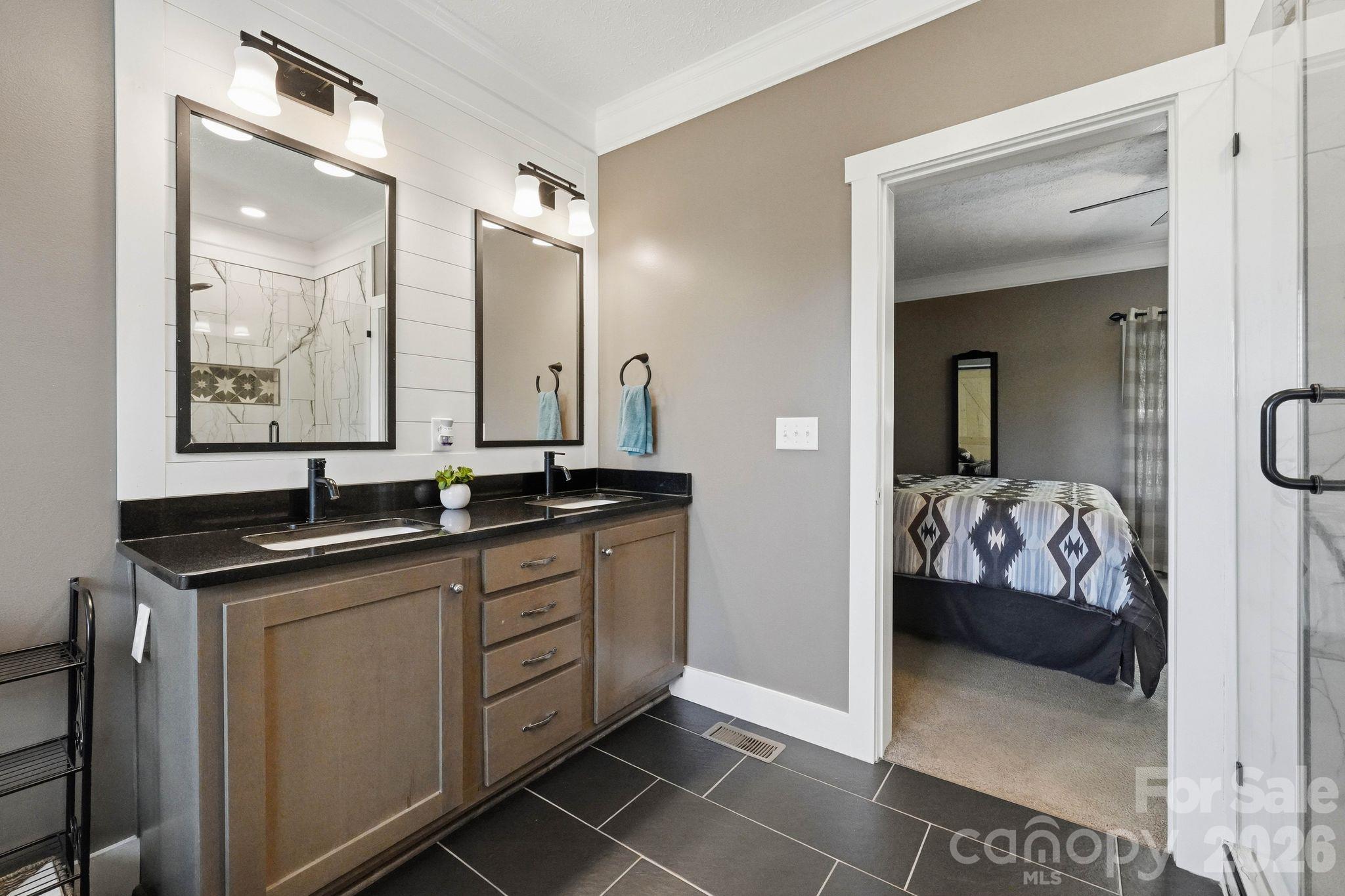 Bathroom with a double-sink vanity and dark tile floor, opening into a bedroom.