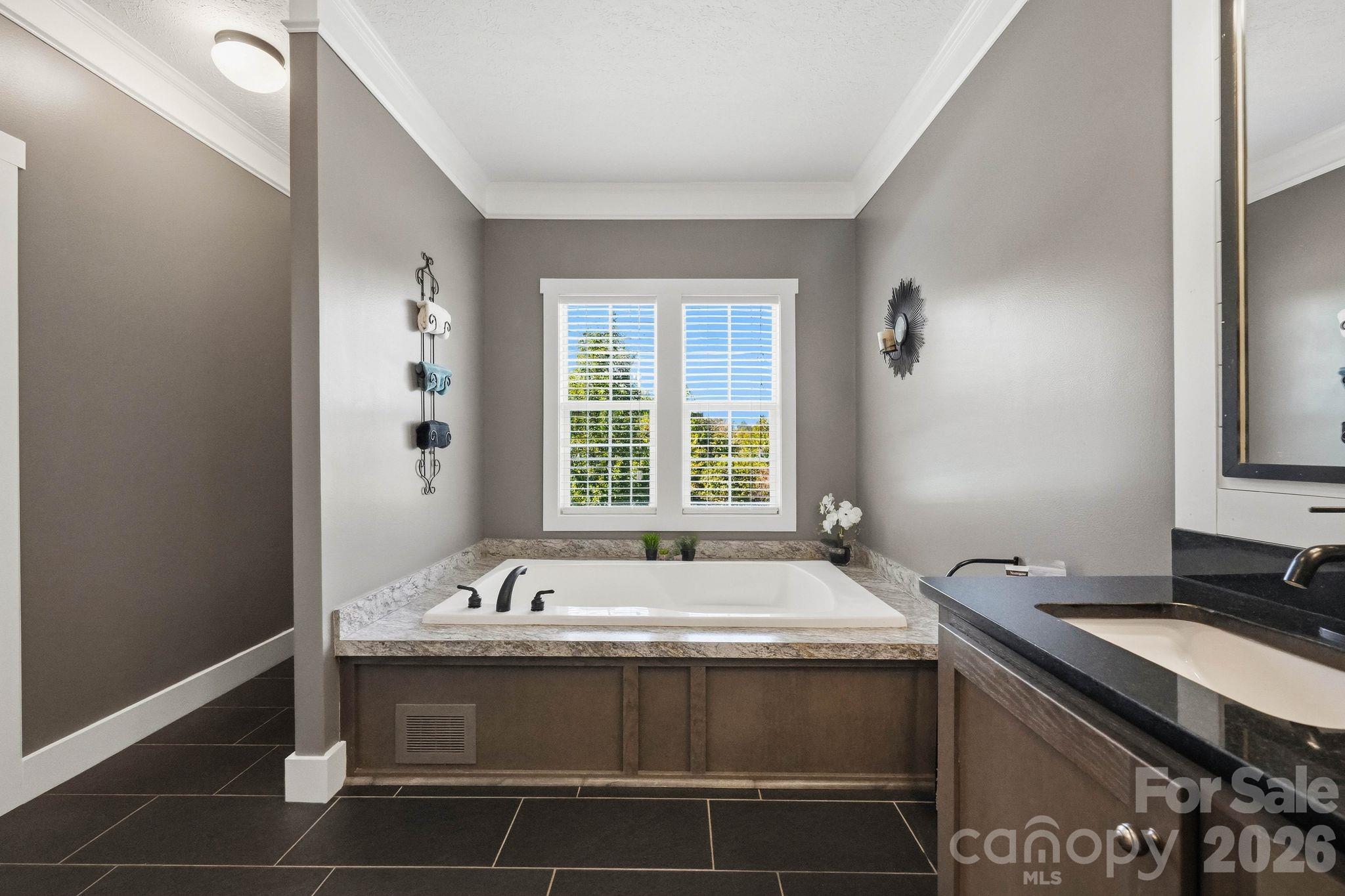 Bathroom with a built-in soaking tub beneath a double window and a granite vanity.