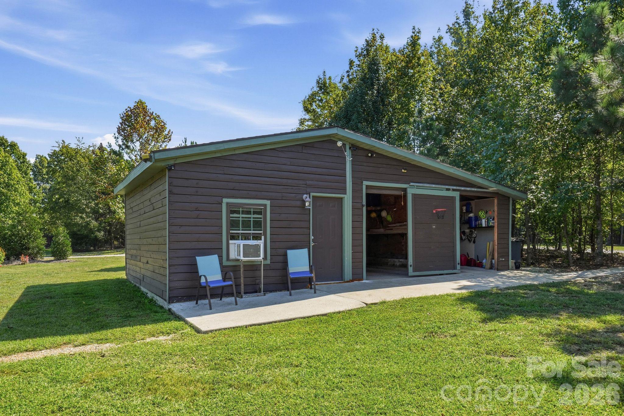 Detached brown garage with open storage bays, a concrete apron, and a grassy yard.
