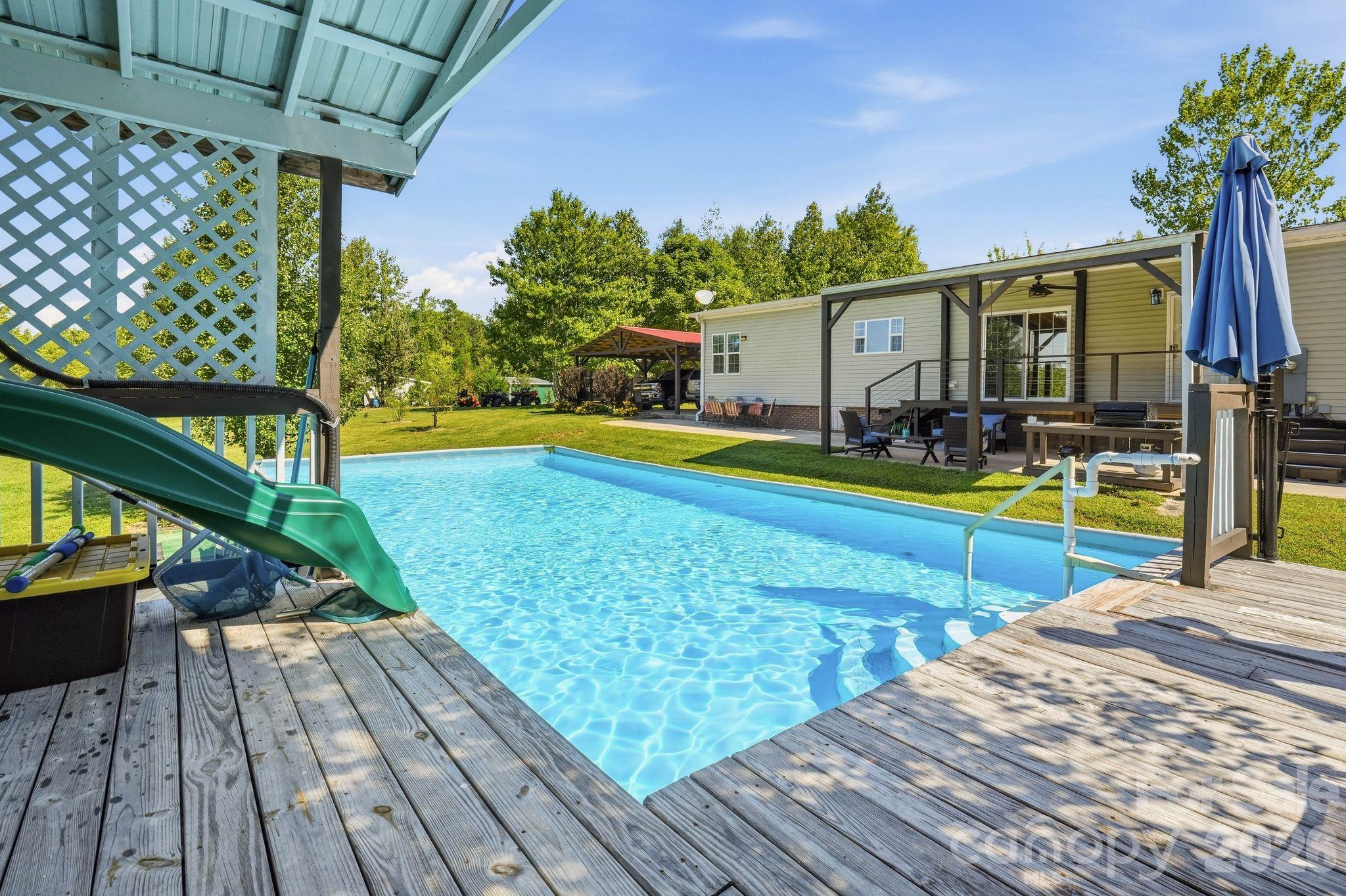 Backyard pool bordered by wooden decks, with a green slide and covered patio.