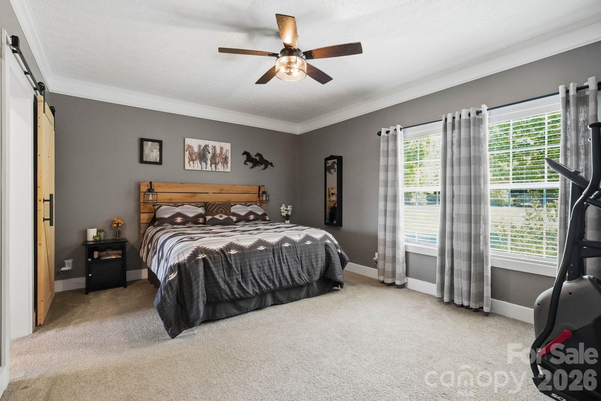 Bedroom with gray patterned bedding, a wood plank headboard, and large curtained windows.