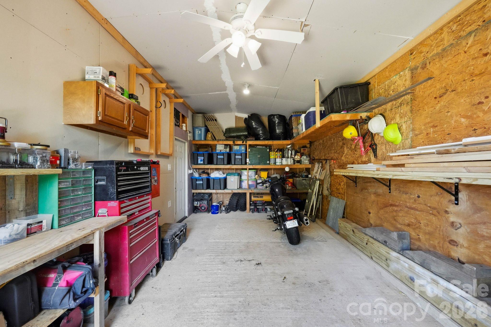 Garage workshop with red tool chests, stocked shelves, lumber, and a motorcycle.