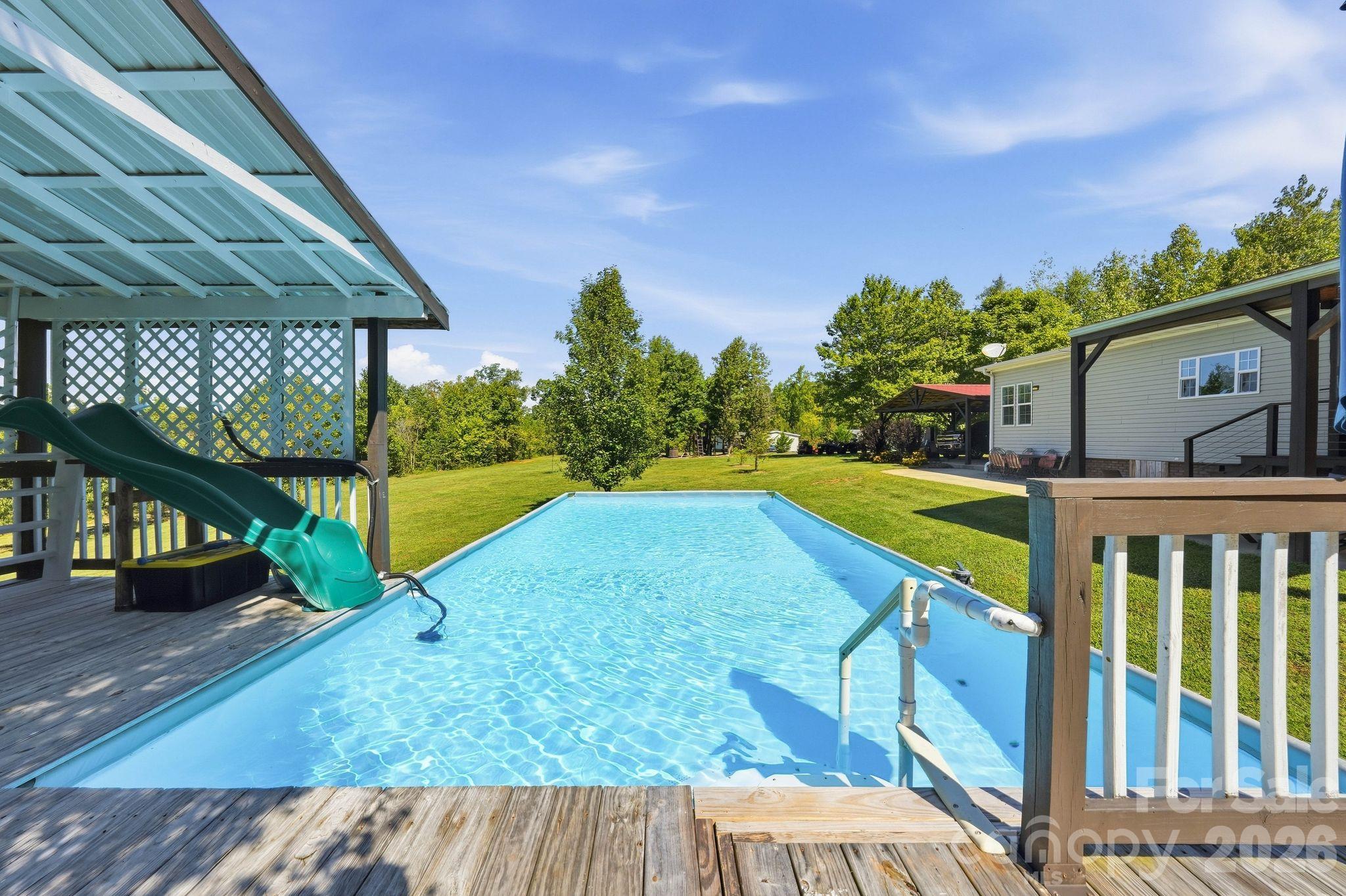 Backyard swimming pool with a wooden deck and a play structure with a green slide.