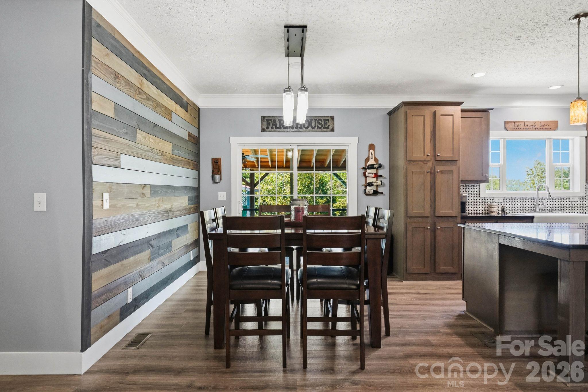 Dining area with a multitone wood-plank accent wall, dark table, and adjoining kitchen island.