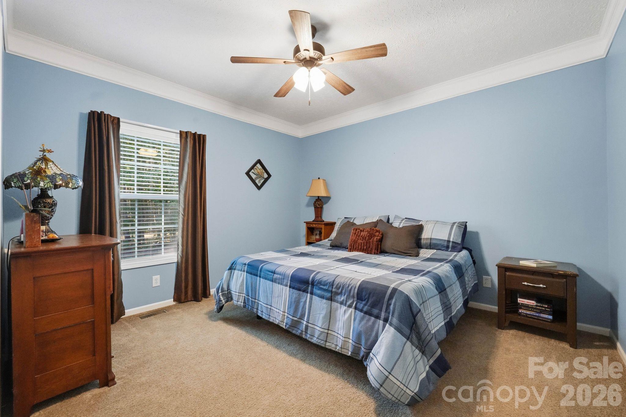 Bedroom with a large bed in blue plaid bedding, pale blue walls, and dark window curtains.