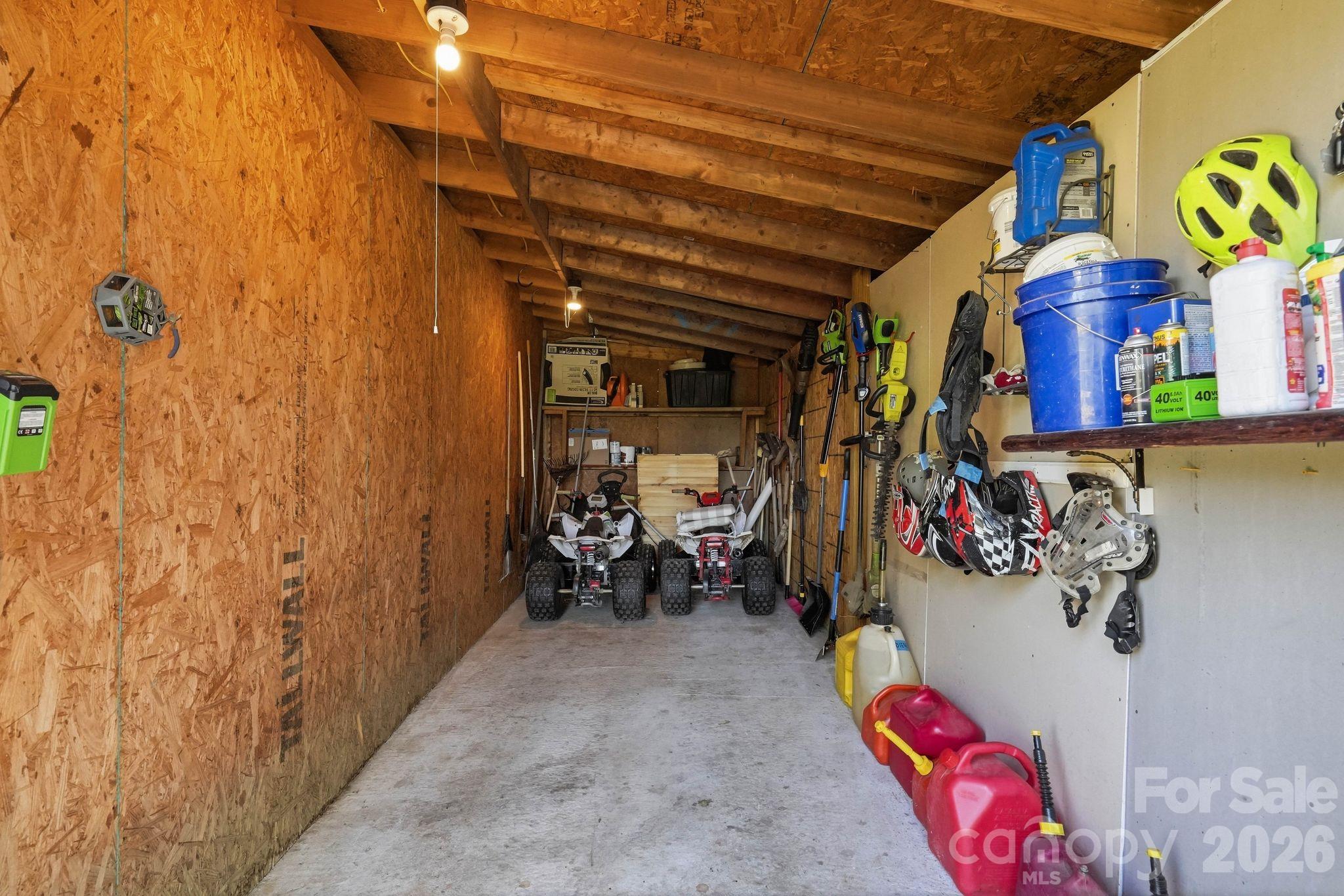 Unfinished wooden garage with two small off-road vehicles, tools, and sports gear in storage.