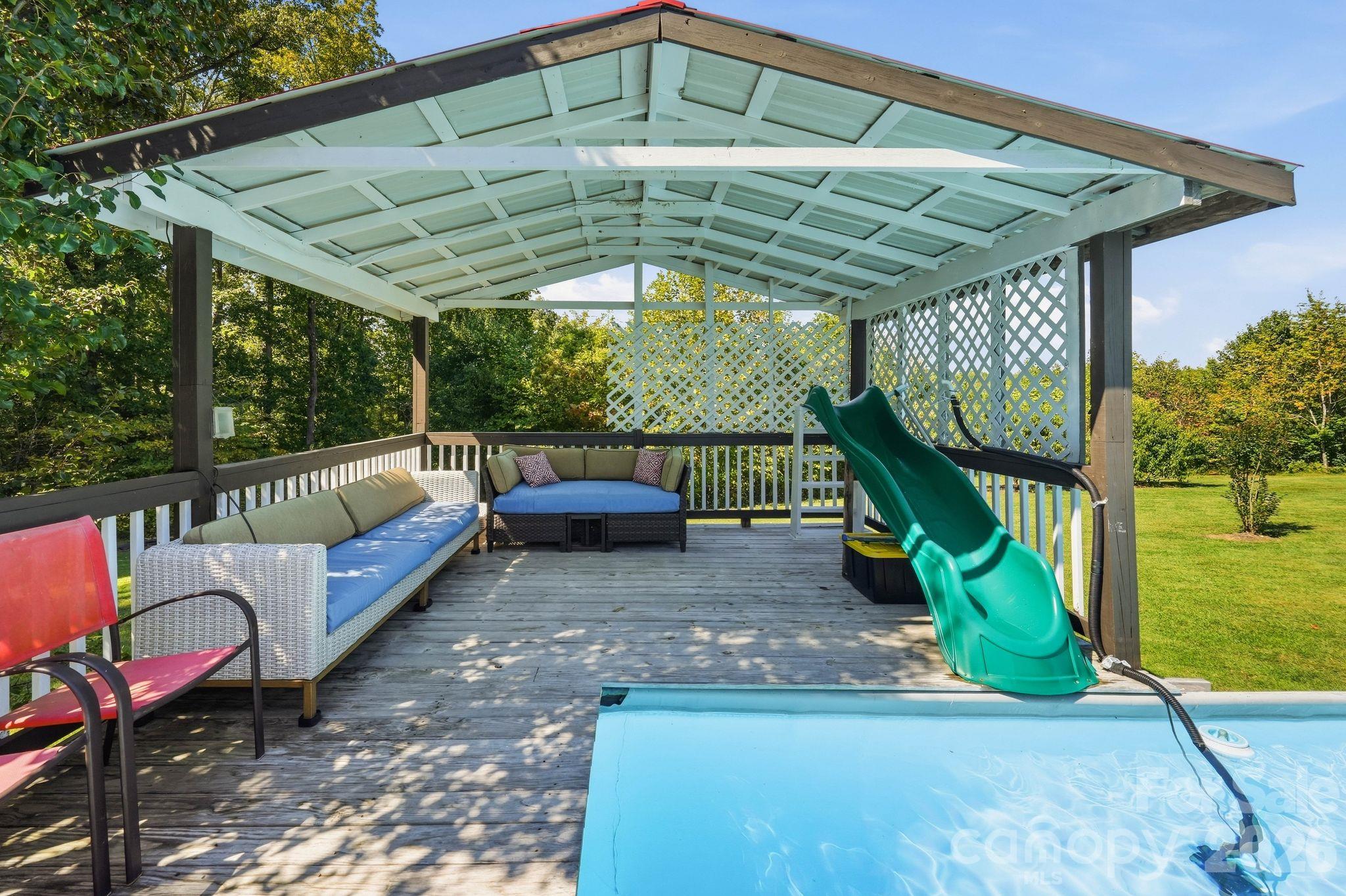 Covered pool deck with wicker seating and a green slide descending into the pool.