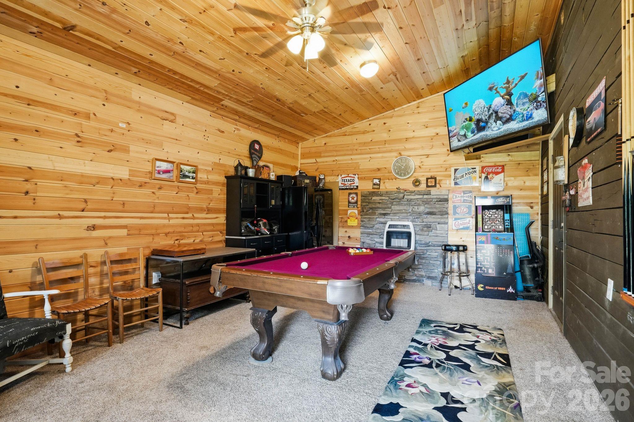Wood-paneled game room with a magenta pool table, stone fireplace, and arcade games.