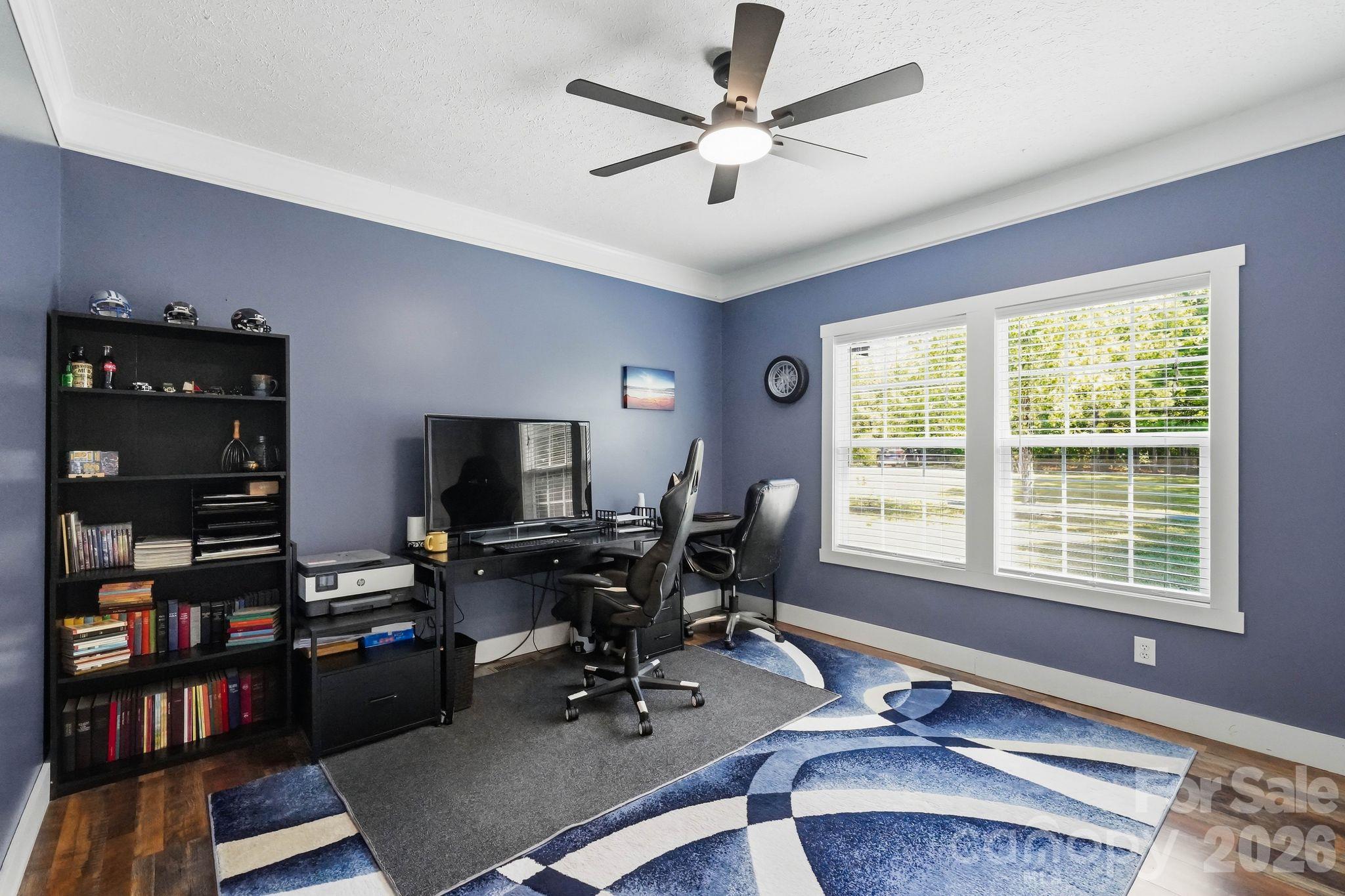 Furnished home office with two computer desks, gaming chairs, a black bookcase, and a blue patterned rug.