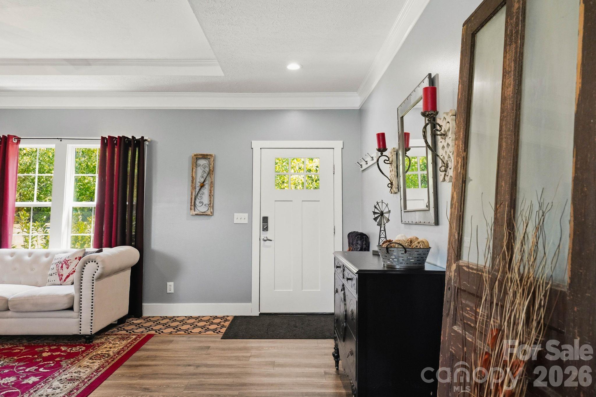 Staged entryway with a white front door, tufted sofa, burgundy curtains, and a black console.