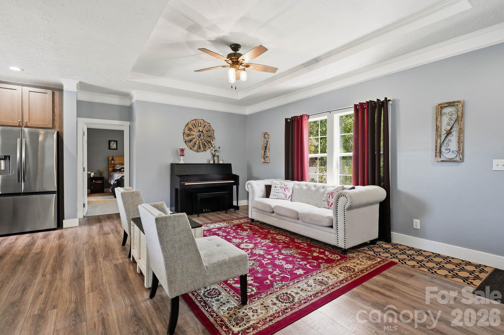 Living room with a black piano, white sofa, and red patterned rug beside the kitchen.