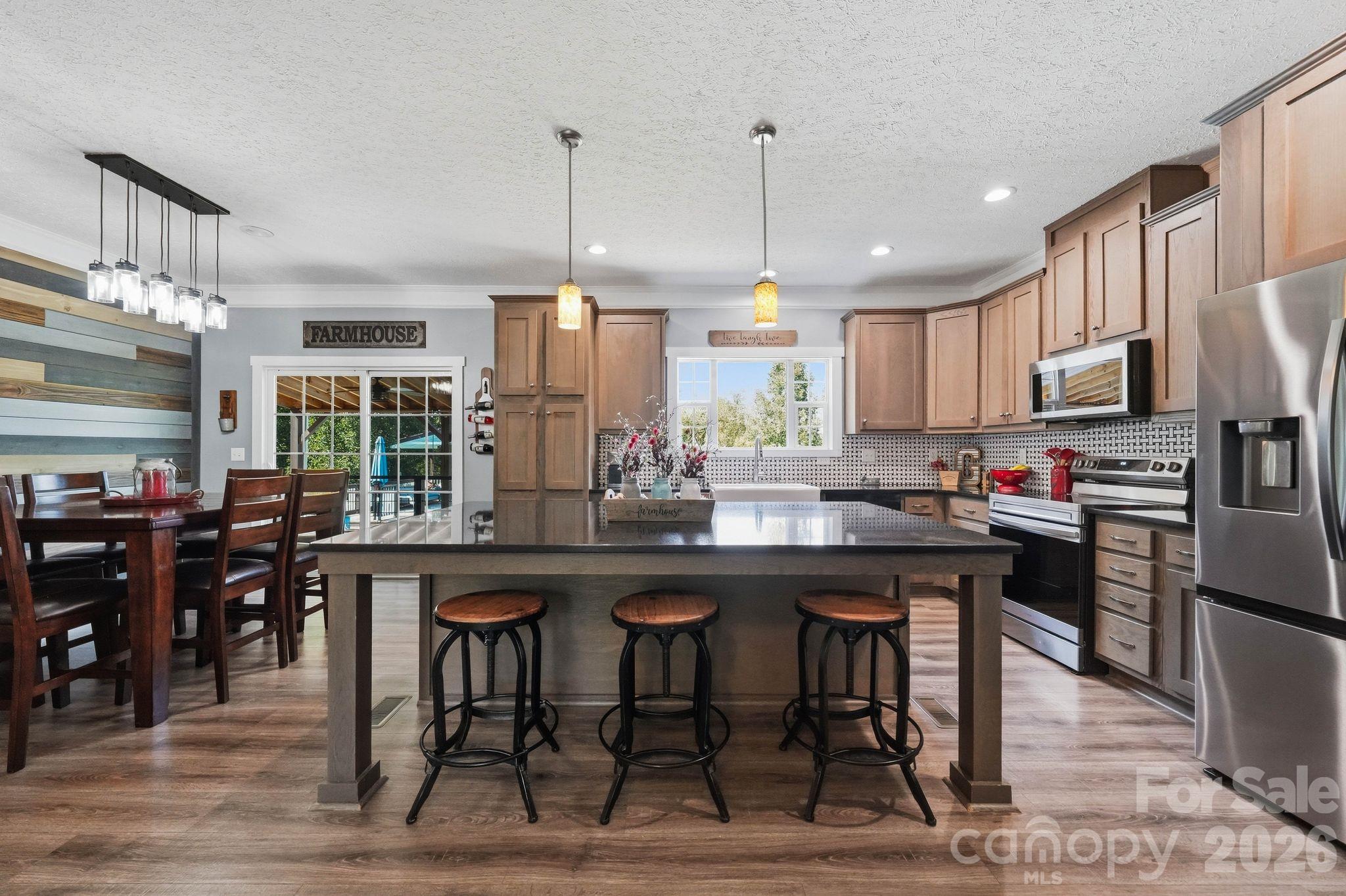 Farmhouse-style kitchen with a large island, three stools, warm wood cabinets, and stainless steel appliances.