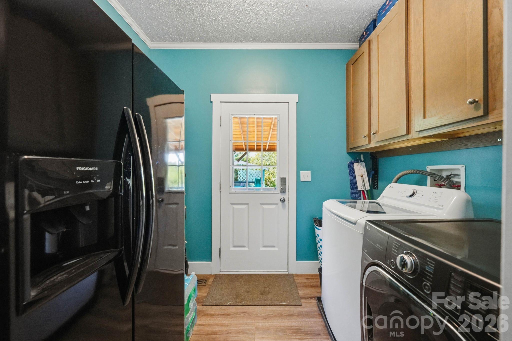 Laundry room with turquoise walls, wooden cabinets, washer and dryer, and a windowed exterior door.
