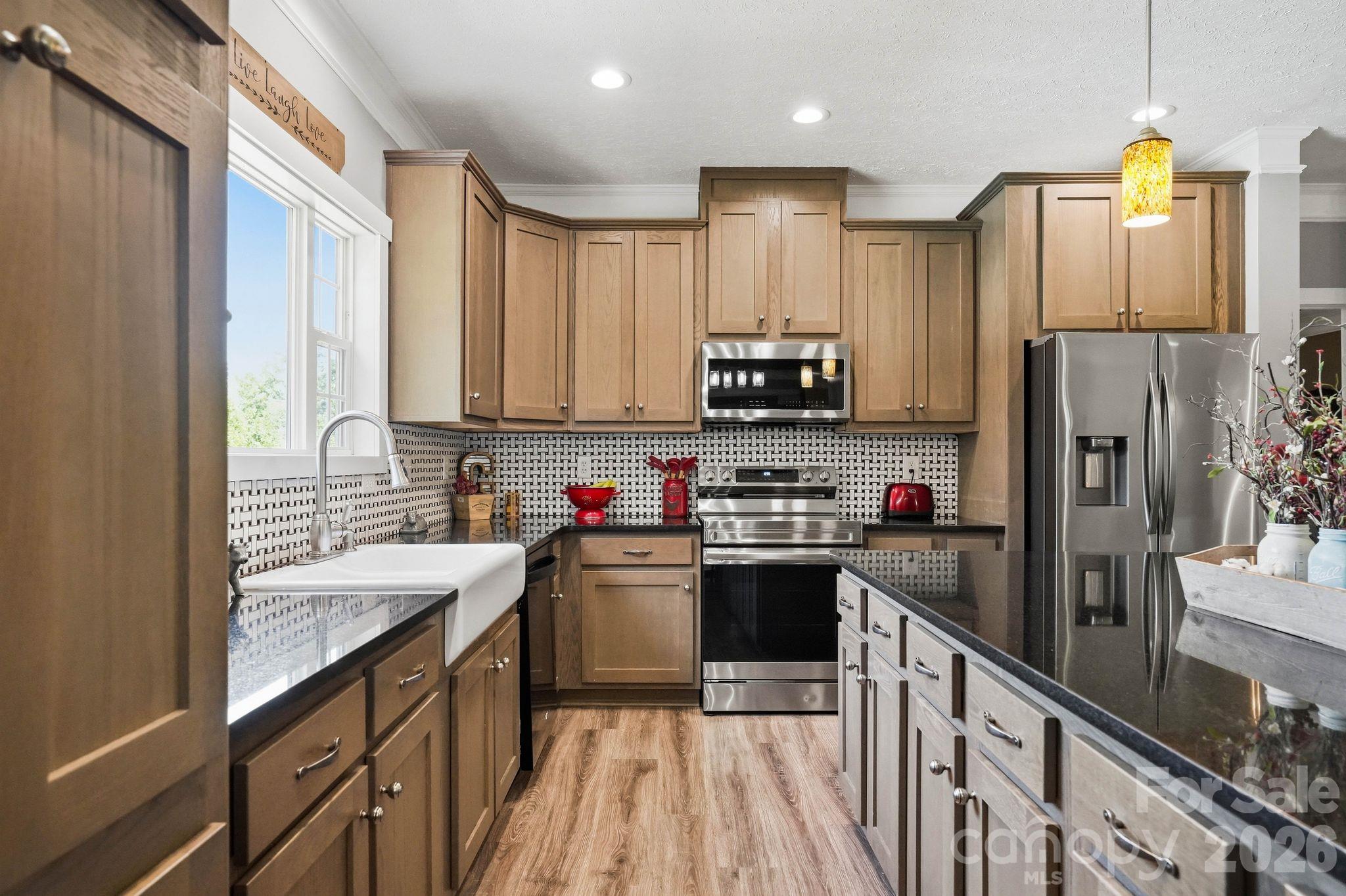 Kitchen with warm wood cabinets, geometric tile backsplash, farmhouse sink, and stainless steel appliances.
