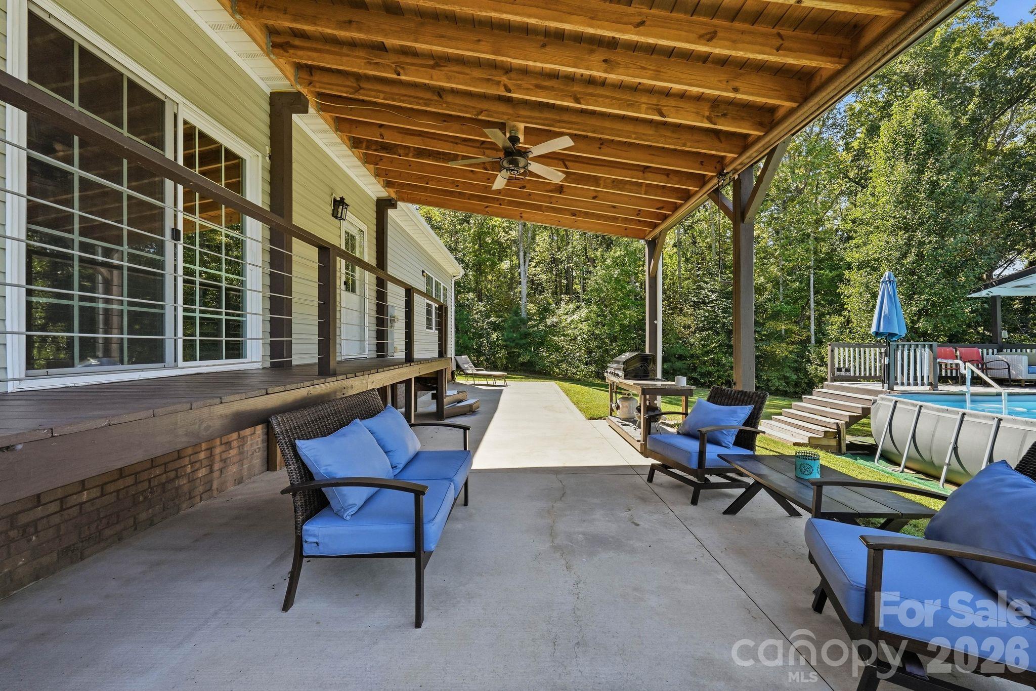 Covered patio with wood ceiling and blue seating beside a backyard above-ground pool.