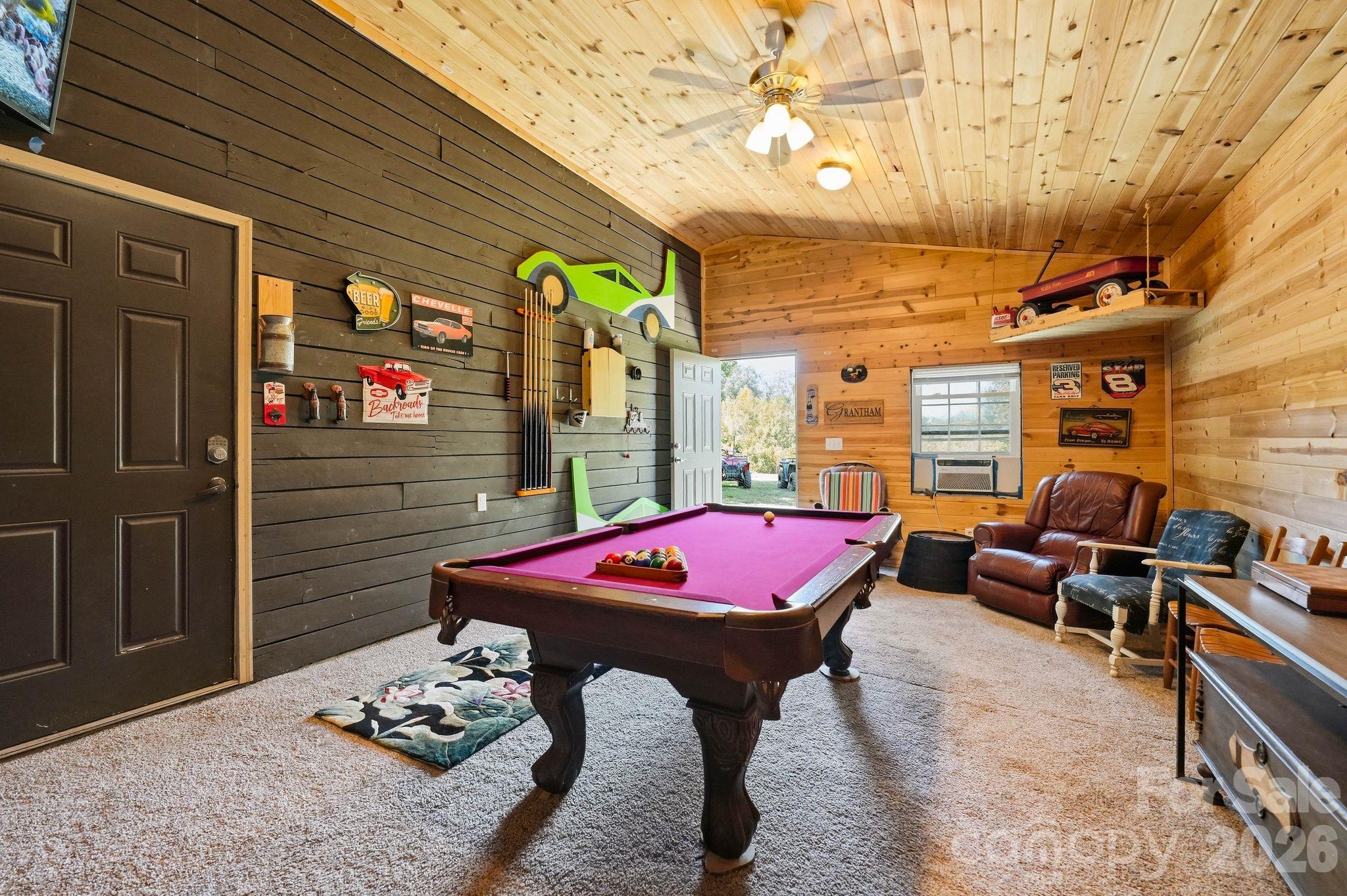 Game room with a magenta-felt pool table, wood-paneled walls, car memorabilia, and leather seating.