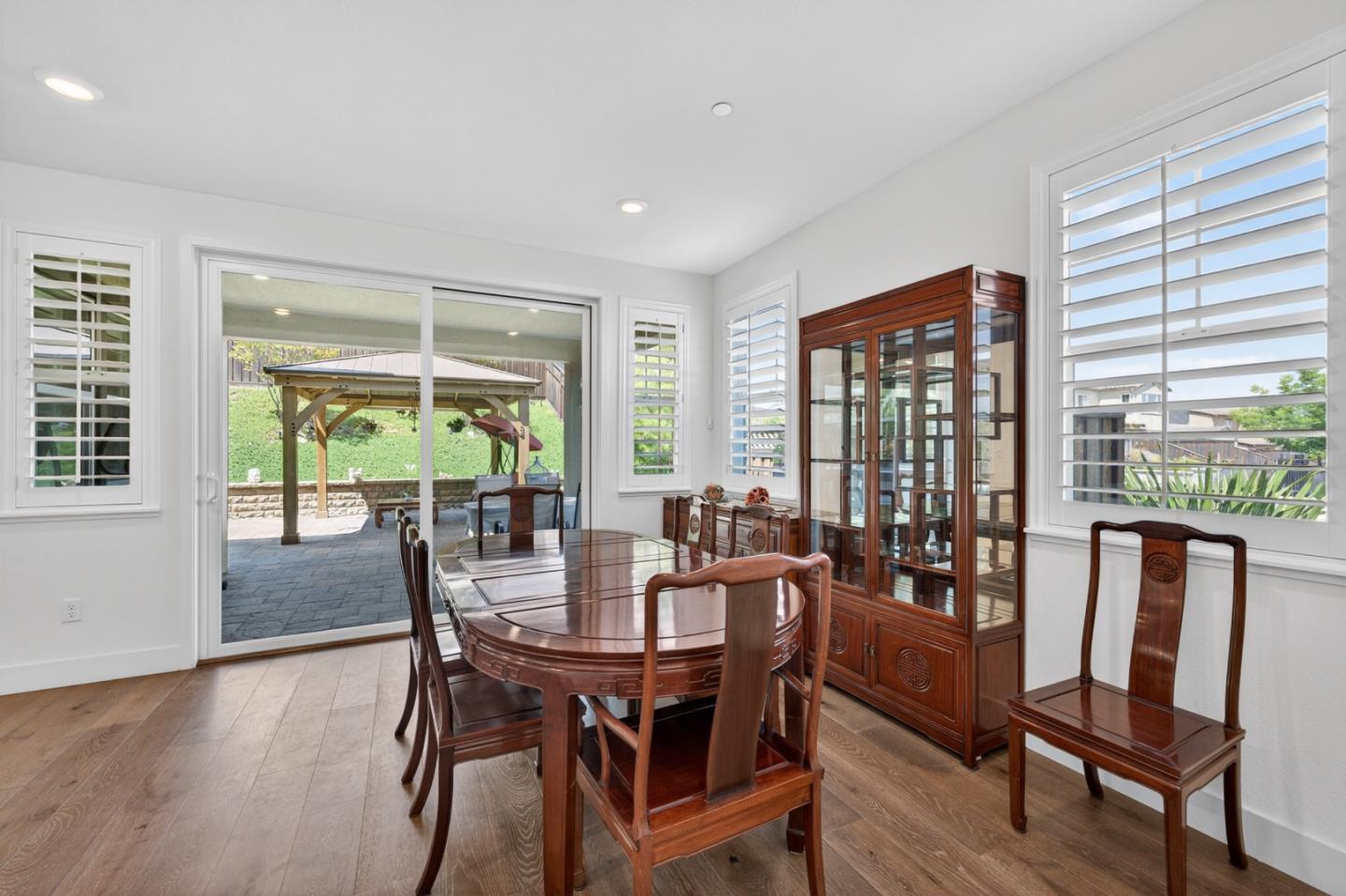 Dining room with a polished wood table, china cabinet, and sliding doors to a pergola patio.