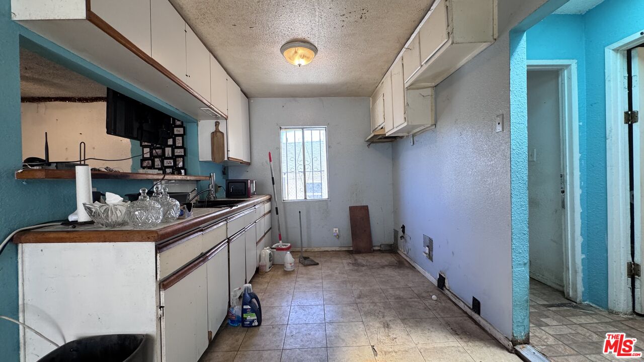 Long, narrow kitchen at 1065 N Gage Ave with white cabinets, a dark countertop, turquoise trim, tiled floor, and a window at the far end.