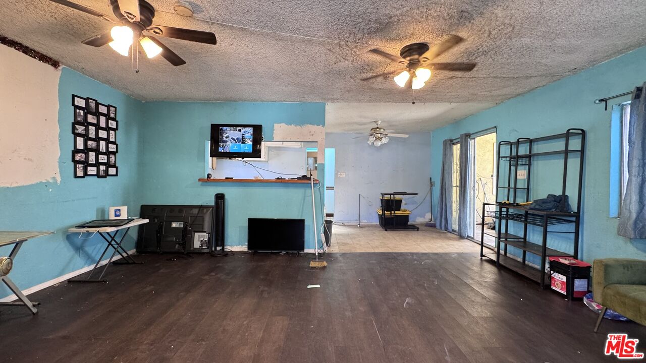 Spacious living area at 1065 N Gage Ave with teal walls, dark wood flooring, two ceiling fans, a wall-mounted TV, and open shelving.