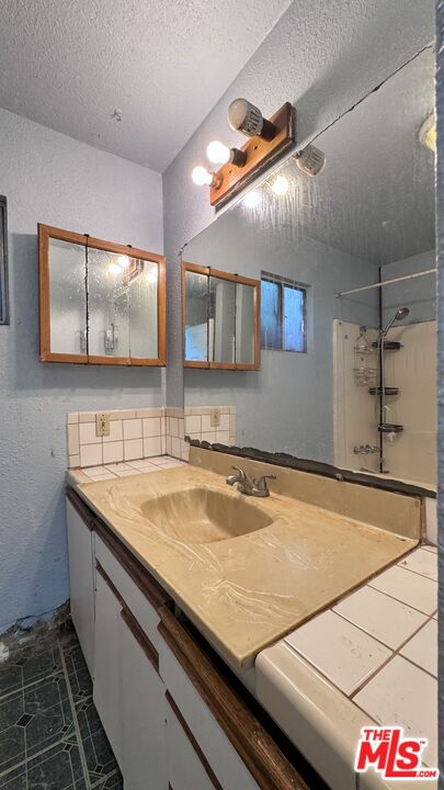 Bathroom vanity with a beige countertop, mirrored medicine cabinets, tiled backsplash, and shower at 1065 N Gage Ave.
