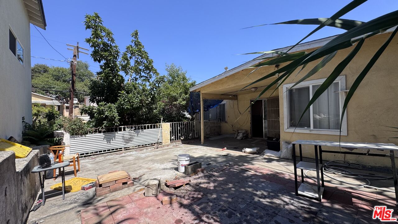 Concrete courtyard beside the single-story home at 1065 N Gage Ave, with a covered patio, metal table, and shaded seating area.