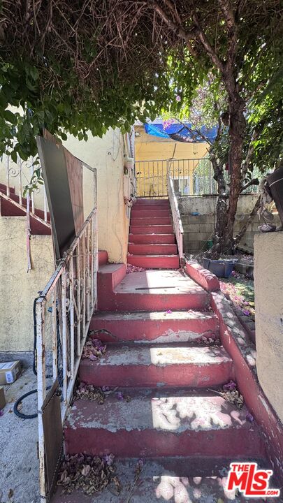 Red concrete stairs lead up to the entrance of 1065 N Gage Ave, shaded by overhanging trees.