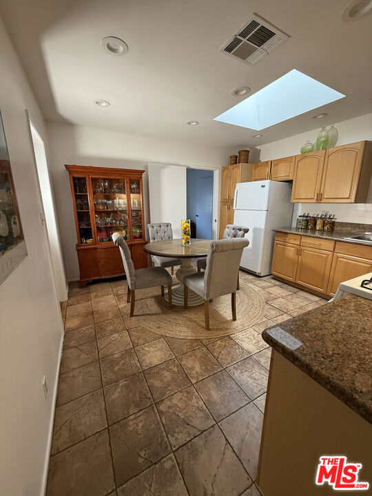 Kitchen and dining area at 2643 S Spaulding Avenue, with a skylight, wood cabinetry, white refrigerator, tiled floor, and round table with four chairs.