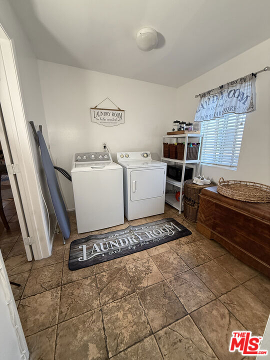 Laundry room at 2643 S Spaulding Avenue with a white washer and dryer, storage shelves, a window with blinds, and brown tile flooring.