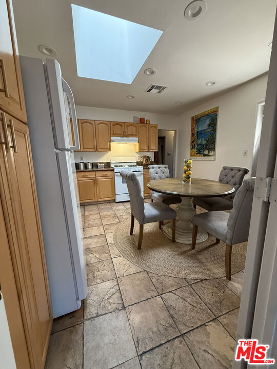 Kitchen and dining area at 2643 S Spaulding Avenue, with oak cabinets, stainless-steel appliances, a skylight, and a round table surrounded by upholstered chairs.