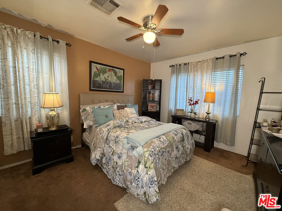 Bedroom at 2643 S Spaulding Avenue with a floral bedspread, two curtained windows, bedside tables, and a ceiling fan.