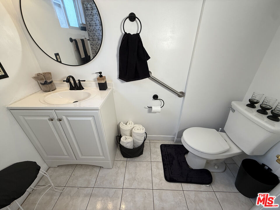 Bathroom at 2643 S Spaulding Avenue with a white vanity and round mirror, toilet, wall-mounted grab bar, and light tile flooring.